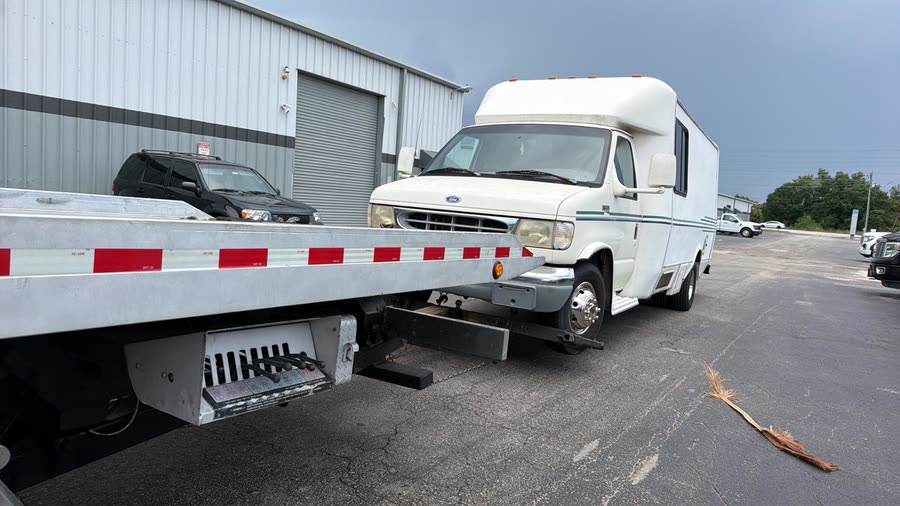 Small camper van on the flatbed outside a repair shop