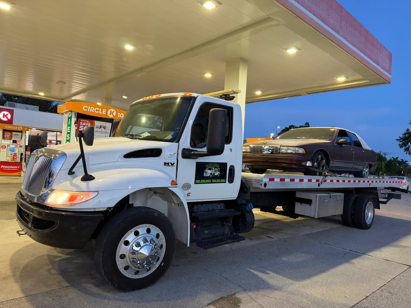 Brayan Towing truck loading a car at dusk at a gas station